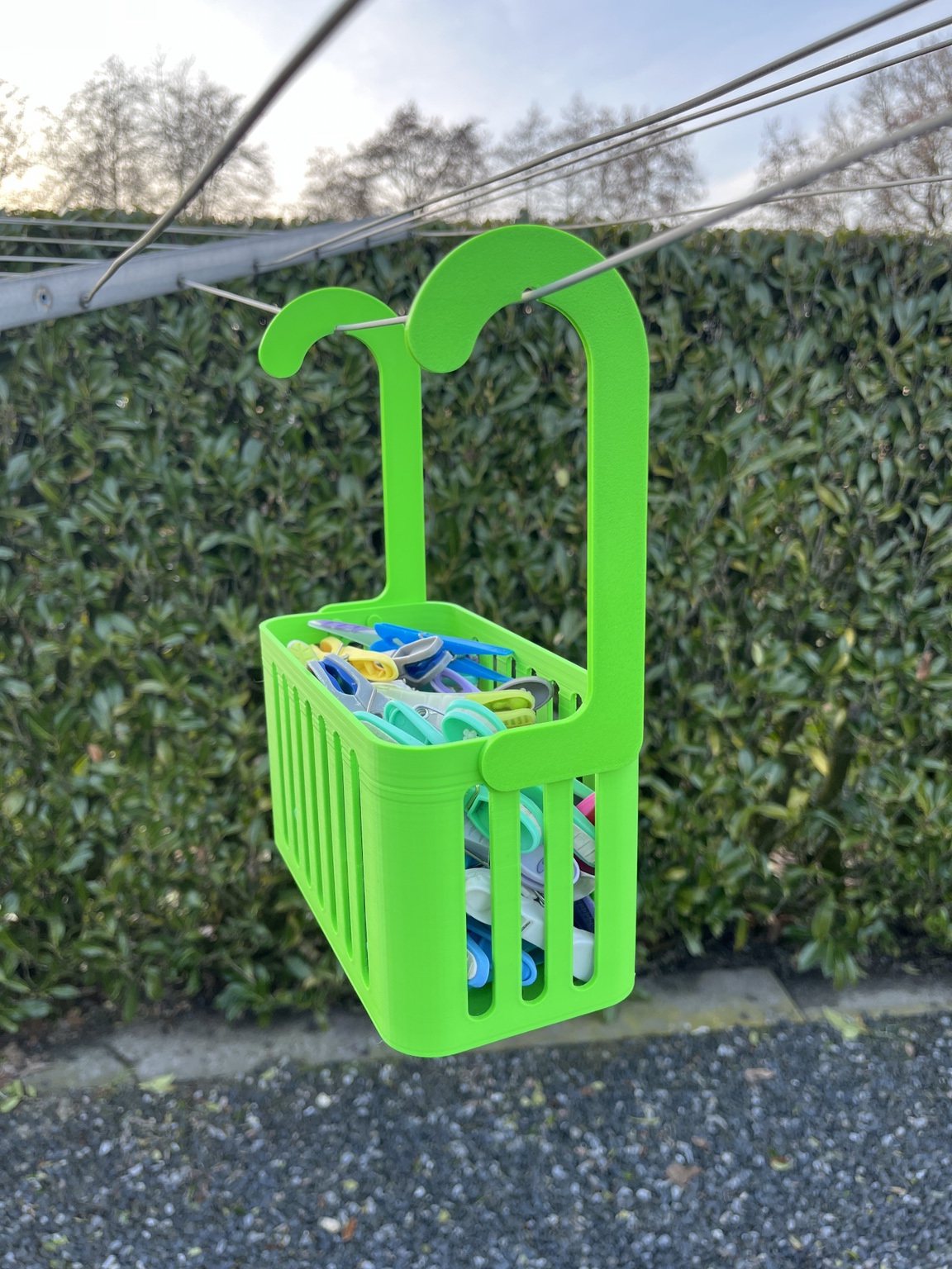 Groen PETG knijpermandje met twee ophanghaken, gevuld met knijpers aan een droogmolen